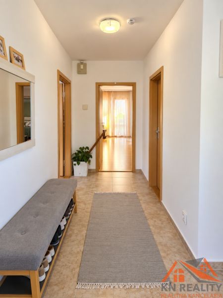 Folyosó egy családi házban csempével, cipőspaddal és tükörrel.