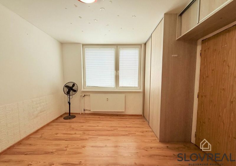 Szoba fa dekorációs padlóval, ventilátorral és tárolóhellyel egy háromszobás lakásban.