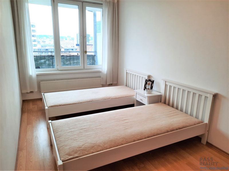 Hálószoba két ággyal, éjjeliszekrénnyel és fa dekoros padlóval egy kétszobás lakásban.