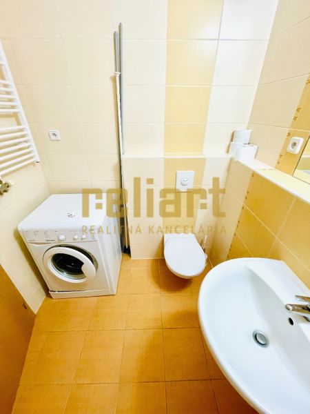 Fürdőszoba egy egyszobás lakásban mosógéppel, mosdóval és WC-vel.