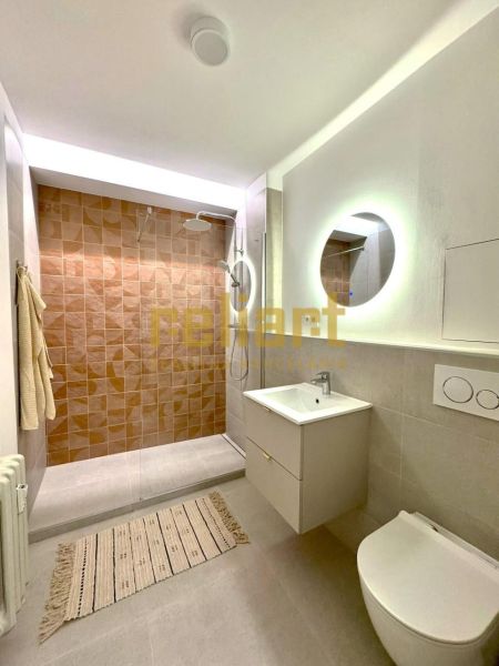 Fürdőszoba walk-in zuhanyzóval, fali WC-vel és megvilágított tükörrel egy garzonlakásban.