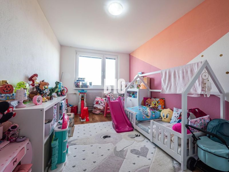 Gyerekszoba egy háromszobás lakásban játékokkal és ággyal, fa dekorációjú padlóval.